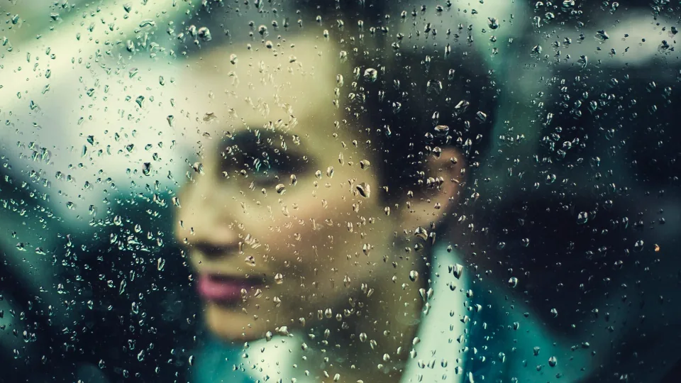 A person looking out through a rain-streaked window, reflecting a low mood