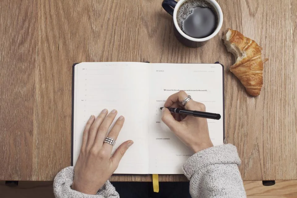 A person journaling in a notebook beside a cup of coffee, a calming daily routine