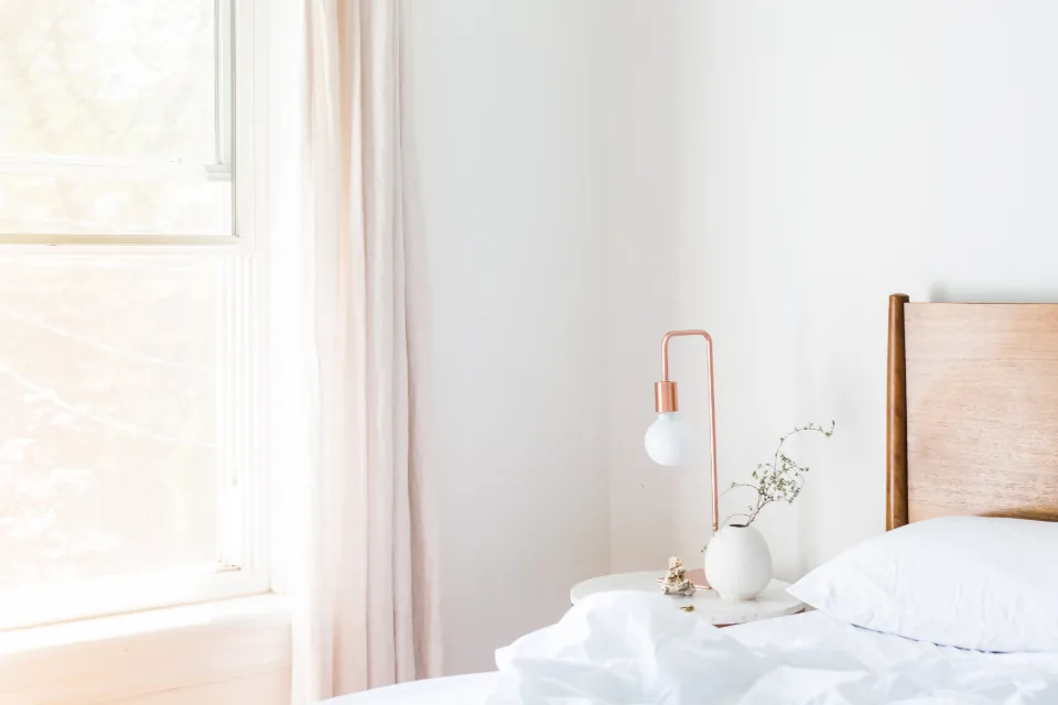 A bright, calm bedroom with a bed and nightstand by a sunlit window