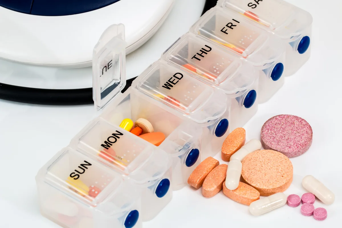 A weekly pill organizer with daily compartments and assorted medications