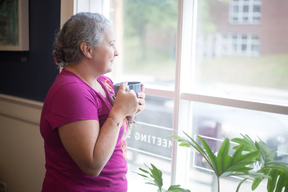 Mature woman holding a warm mug and looking out a window