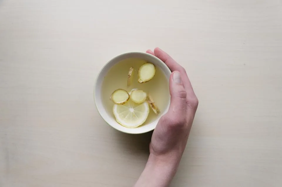 Hands holding a warm cup of ginger and lemon tea while recovering from a respiratory illness